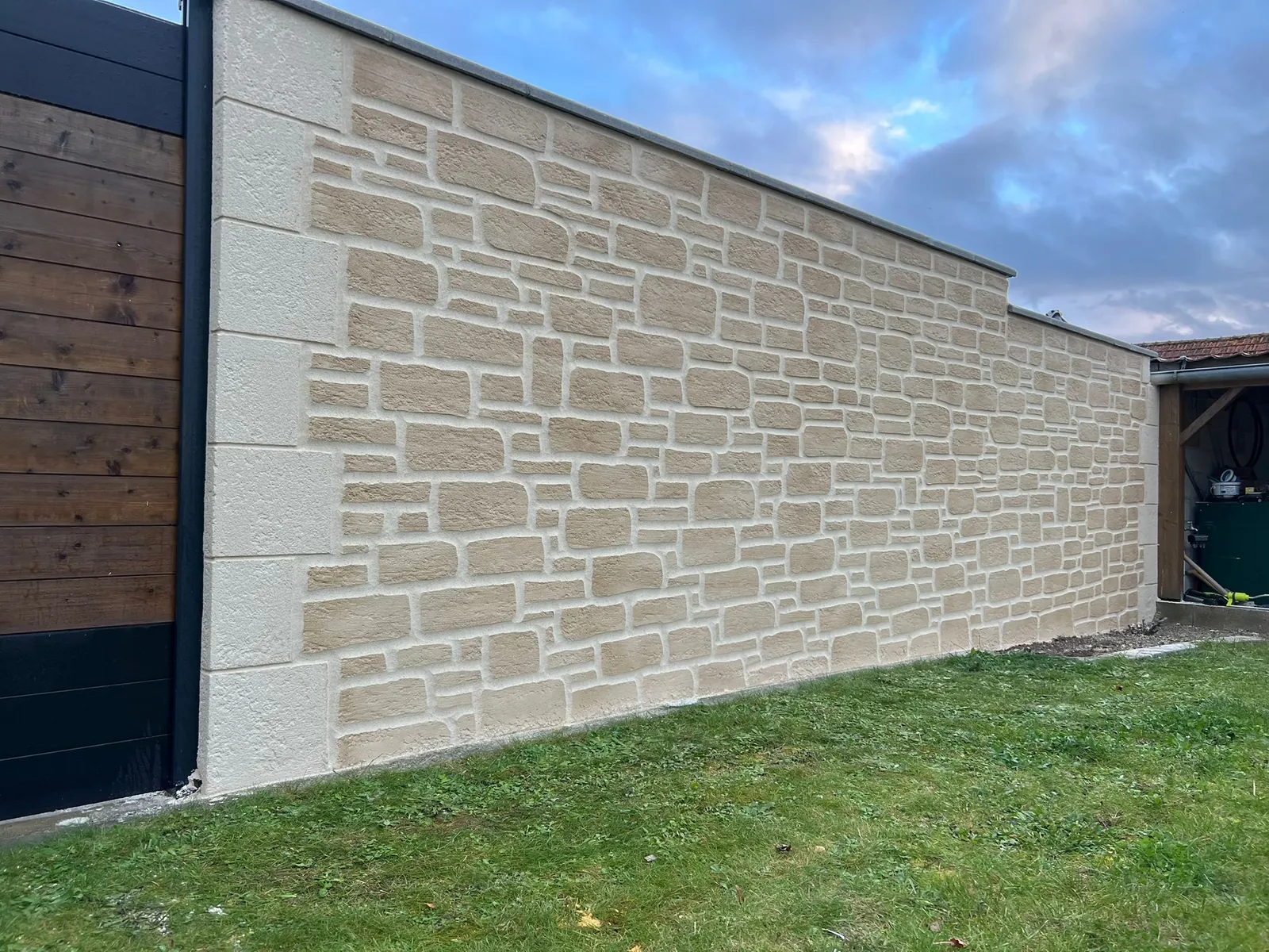 Long mur en imitation pierre le long d'une allée avec portail bois