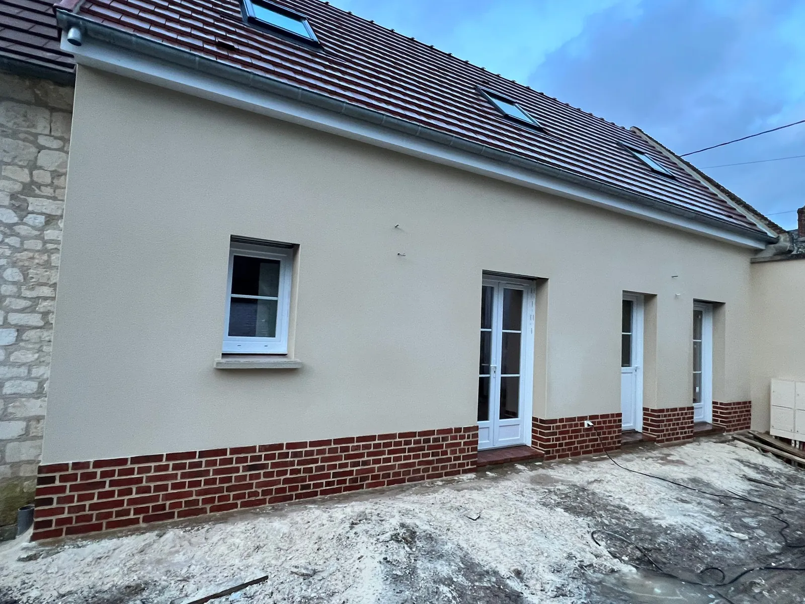 Façade rénovée en enduit clair avec soubassement en brique rouge